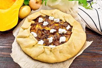 Pie of pumpkin, fried onions and soft cheese on paper, napkin, parsley on a wooden board background
