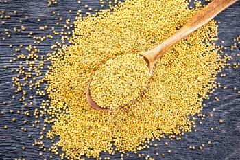 Mustard seeds in a spoon and on a table on the background of a wooden board from above