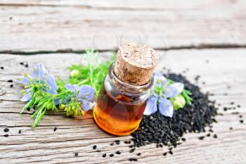 Nigella sativa oil in a bottle, seeds and twigs of black caraway seeds with blue flowers on a wooden board background