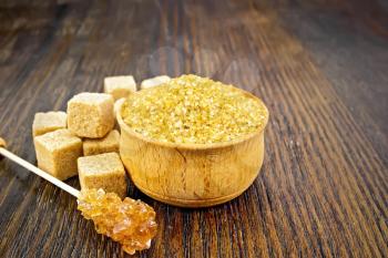Granulated brown sugar in a bowl, crystalline on a stick and diced on a dark wooden board background