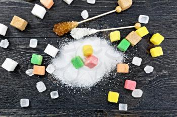 Sugar of white, brown, pink, green, yellow and different shapes on a wooden board background from above