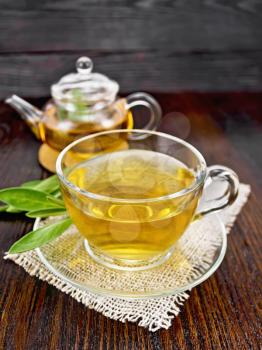Herbal tea with sage in a glass cup and teapot on burlap on a wooden board background