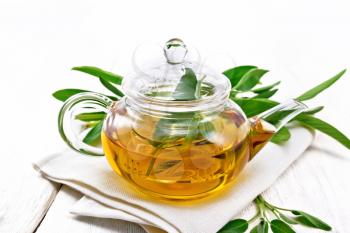 Herbal tea with sage in a glass teapot on a napkin on wooden board background