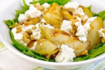 Salad of fried pear, spinach, salted feta cheese and cedar nuts in a plate on a kitchen towel on a wooden plank background
