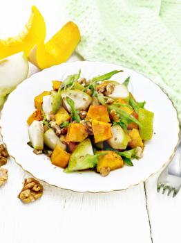 Salad of baked pumpkin, fresh pear, arugula and walnuts, seasoned with honey, balsamic vinegar, spices and vegetable oil in a plate, napkin and fork on background of light wooden board