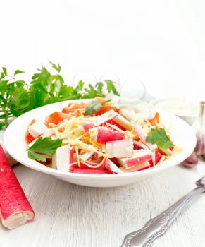 Salad of crab sticks, cheese, garlic, tomatoes and mayonnaise, kitchen towel, parsley on a light wooden board background