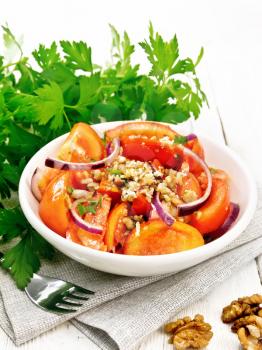 Fresh tomato salad with walnuts and red onions, seasoned with olive oil, vinegar, fenugreek and salt in a plate on a napkin on wooden board background