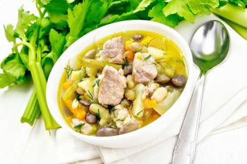 Eintopf soup of pork, celery, beans, carrots and potatoes with leek in a white bowl on a napkin on light wooden board background