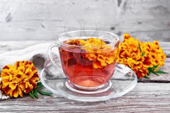Marigold herbal tea in a glass cup and saucer, fresh flowers, sackcloth napkin on the background of an old wooden board