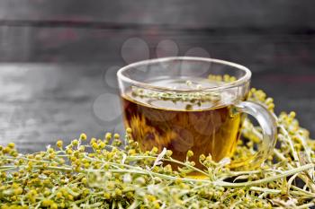 Gray wormwood herbal tea in a glass cup, fresh sagebrush flowers on wooden board background