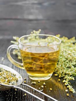 Gray wormwood herbal tea in a glass cup, fresh flowers and metal strainer with dry sagebrush flowers on wooden board background

