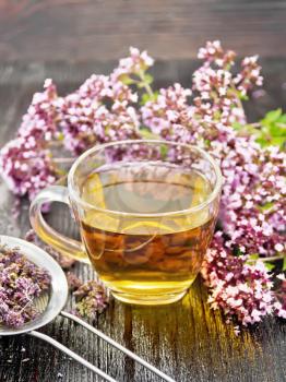 Oregano herbal tea in a glass cup, fresh marjoram flowers and a metal strainer with dried flowers on wooden board background