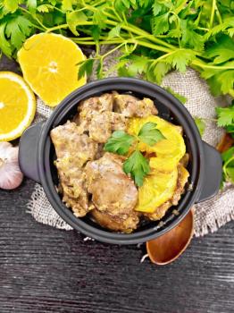 Chicken liver stewed with oranges, sour cream, soy sauce and Provencal herbs in a small saucepan on burlap, a spoon and parsley on wooden board background from above