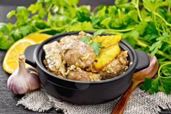 Chicken liver stewed with oranges, sour cream, soy sauce and Provencal herbs in a small saucepan on burlap napkin, spoon and parsley on wooden board background