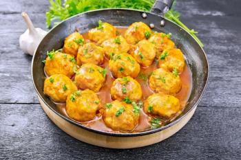 Meatballs with tomato sauce in a frying pan with parsley, dill, napkin and spoon on a wooden board background