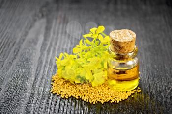 Mustard oil in a glass bottle, grains and yellow flowers on a dark wooden board background
