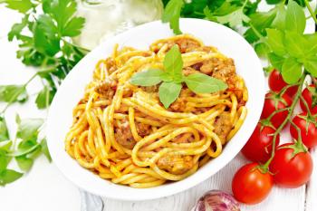 Spaghetti pasta with sauce Bolognese of minced meat, tomato juice, garlic, wine and basil in a plate, vegetable oil, spicy herb on a wooden board background