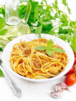 Spaghetti pasta with sauce Bolognese of minced meat, tomato juice, garlic, wine and basil in a plate, vegetable oil, spicy herb on a light wooden board background