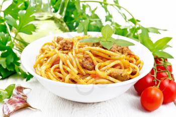 Spaghetti pasta with sauce Bolognese of minced meat, tomato juice, garlic, wine, spices and basil in a plate, vegetable oil, spicy herb on a wooden board background
