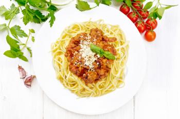 Spaghetti pasta with Bolognese sauce of minced meat, tomato juice, garlic, wine and spices with cheese in a plate, vegetable oil, spicy herb on a wooden board background from above