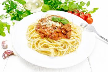 Spaghetti pasta with Bolognese sauce of minced meat, tomato juice, garlic, wine and spices with cheese in a plate, vegetable oil, spicy herb on a wooden board background