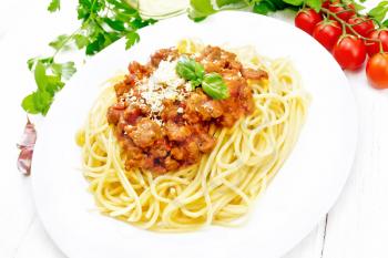 Spaghetti pasta with Bolognese sauce of minced meat, tomato juice, garlic, wine and spices with cheese in a plate, vegetable oil, spicy herb on a white wooden board background
