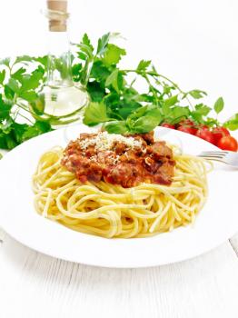 Spaghetti pasta with Bolognese sauce of minced meat, tomato juice, garlic, wine and spices with cheese and fork in a plate, vegetable oil, spicy herb on a white wooden board background