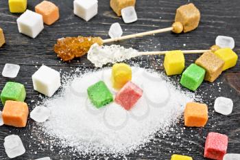Sugar of white, brown, pink, green, yellow and different shapes on a black wooden board background
