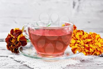 Marigold herbal tea in a glass cup and saucer on a napkin of sackcloth, fresh flowers on wooden board background
