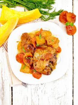 Chicken stew with pumpkin, dried apricots, carrots and red wine, sprinkled with sesame seeds in a plate on a napkin against wooden board on top