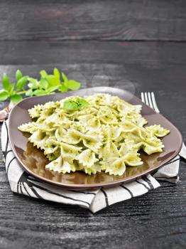 Farfalle pasta with pesto, basil in a plate on a napkin on wooden board background