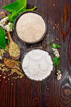 Buckwheat flour from green and brown cereals in two bowls, groats in spoons and on the table, flowers and buckwheat leaves on the background of a wooden board from above
