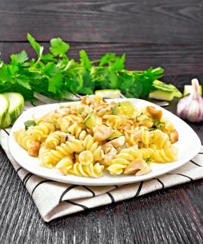 Fusilli pasta with chicken breast, zucchini, cream and pine nuts in a plate on napkin, garlic, fork and parsley on a wooden board background