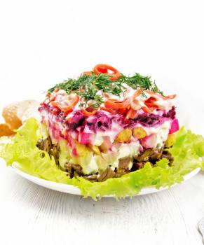 Puff salad with beef, potatoes and beets, pears, Korean spicy carrots, seasoned with mayonnaise and garnished with dill on a green lettuce in a plate, towel, bread on wooden board background