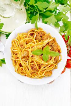 Spaghetti pasta with sauce Bolognese of minced meat, tomato juice, garlic, wine and basil in a plate, vegetable oil, spicy herb on a light wooden board background from above
