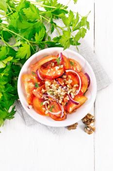 Fresh tomato salad with walnuts and red onions, seasoned with olive oil, vinegar, fenugreek and salt in a plate on a towel on light wooden board background from above