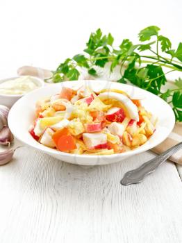 Salad of crab sticks, cheese, garlic, tomatoes and eggs with mayonnaise in a plate, napkin, parsley and fork on a light wooden board background