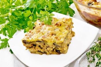 Casserole of minced meat, onion and eggplant doused with a sauce of eggs, milk, cheese and flour in a plate on towel against wooden board background