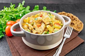 Stew of chicken breast, tomatoes, stalked celery, carrots, green peas and onions in a tureen on a napkin against dark wooden board