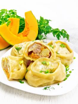 Manty steamed pies with minced meat and pumpkin, green onions in a plate, kitchen towel, parsley and fork on light wooden board background