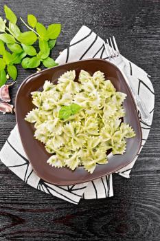 Farfalle pasta with pesto, basil in a plate on a napkin on wooden board background from above