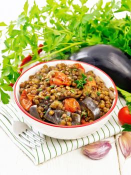 Green lentils stewed with eggplant, tomatoes, garlic and spices in a bowl on a napkin, parsley on light wooden board background
