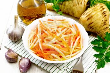 Salad of fresh carrots, parsnip and garlic with vegetable oil in a plate on a napkin, fork, parsley and root vegetables on white wooden board background