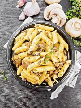 Penne pasta with wild mushrooms in a plate on a kitchen towel, thyme, fork and garlic on wooden board background from above