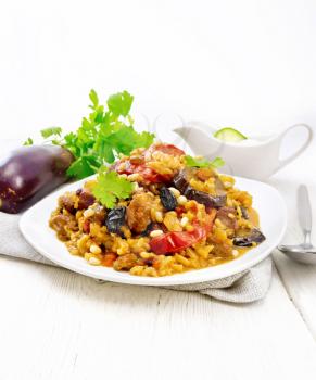 Eastern and European national dish of maklube made of rice, eggplant, tomatoes, spices and garlic in a plate on a napkin on white wooden board background