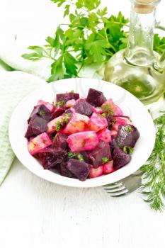 Beetroot and potato salad, seasoned with vegetable oil and vinegar in a plate, napkin, fork, parsley and dill on a white wooden board background