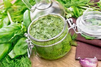 Sauce of dill, parsley, basil, cilantro, other spicy herbs, garlic and vegetable oil in a glass jar, napkin on the background of an old wooden board