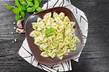 Farfalle pasta with pesto, basil in a plate on a napkin on the background of dark wooden board from above