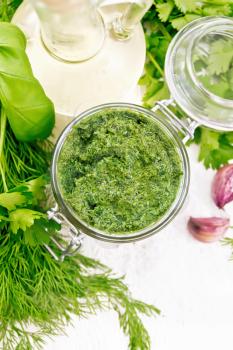 Sauce of dill, parsley, basil, cilantro, other spicy herbs, garlic and vegetable oil in a glass jar, coarse salt on the background of light wooden board from above