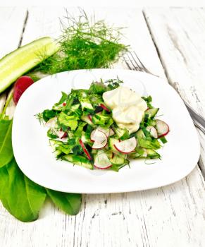 Salad of radish, cucumber, sorrel and greens, dressed with mayonnaise in a plate on the background of wooden board